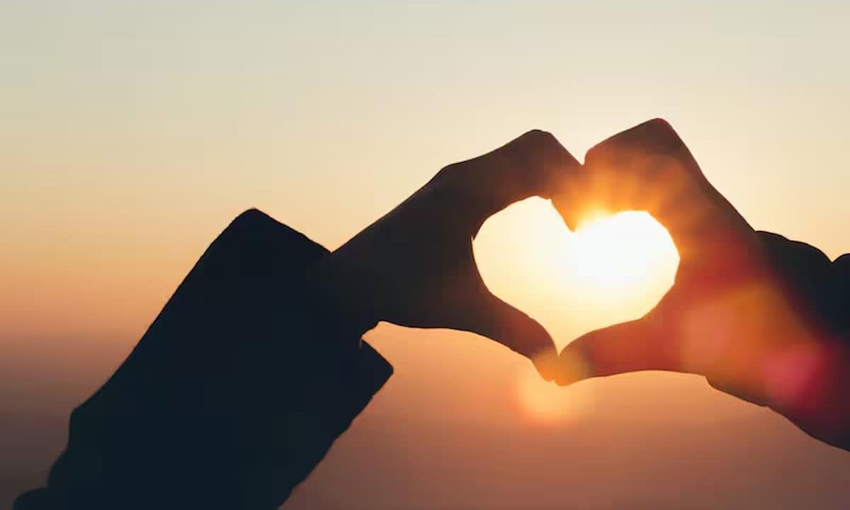 hands making heart over sunset